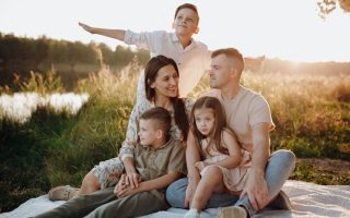 A family of five enjoying a serene picnic in a sunlit meadow during sunset.