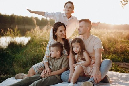 A family of five enjoying a serene picnic in a sunlit meadow during sunset.